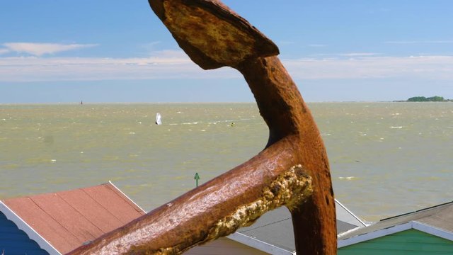 Windsurfer at Mersea Island, with a rusty anchor in the foreground, and a view of beach huts