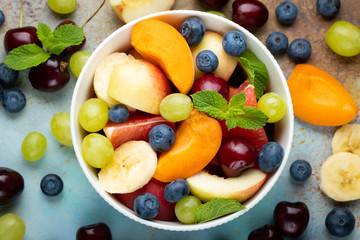Fototapeta na wymiar Bowl of healthy fresh fruit salad on a blue rusty background. Top view