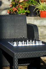 chessboard with black and white figures on the black rattan table under sunlights.