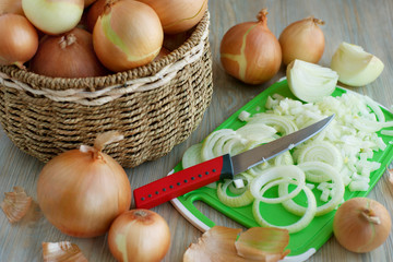 Onions in a basket and chopped. Many onions in a wicker basket. Sliced onions on a cutting board for cooking dishes. Preparation of vegetables for the dish.