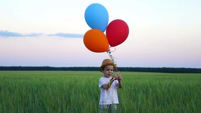 boy of two years standing in the field and releasing balloons into the sky