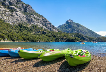 Fototapeta na wymiar Colorful Kayaks in a lake surrounded by mountains at Bahia Lopez in Circuito Chico - Bariloche, Patagonia, Argentina