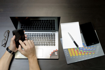 A man prints on a laptop, lying next to the phone, tablet glasse