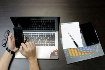 A man prints on a laptop, lying next to the phone, tablet glasse