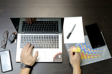 A man prints on a laptop, lying next to the phone, tablet glasse