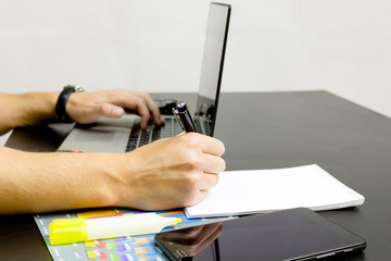 A man prints on a laptop, lying next to the phone, tablet glasse