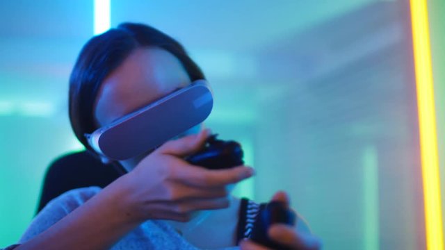 Pro Gamer Girl Wearing Virtual Reality Headset Plays Online Video Game with Joysticks / Controllers. Cool Retro Neon Colors in the Room.