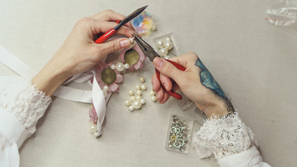 Girl makes fashion jewelry. Shooting close-up. She fixes the fastenings on the decoration with...
