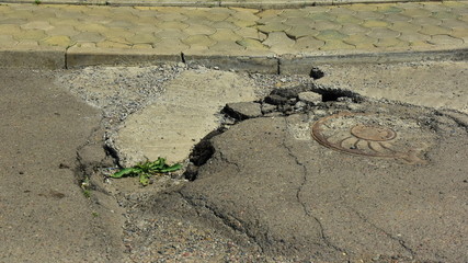 Failure of the asphalt covering next to the sewer hatch. Broken coating. Poor motor road construction