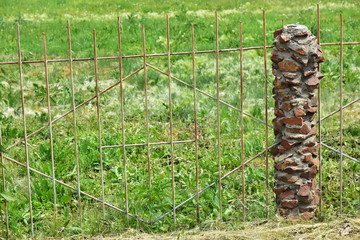 Rustic fence made of light steel grating on a stone pillar. Landscaping on the country side