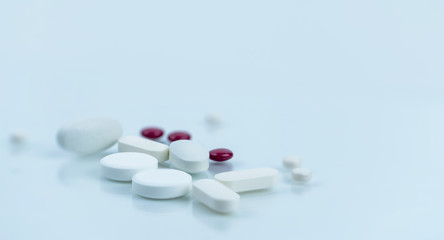 Selective focus on pile of white and red sugar coated tablets pills on blurred background. Pharmacy background. Pharmaceutical industry. Healthcare and pharmacology concept. Drugs on white background