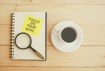 Focus on your goal text on notepad with magnifying glass and cup of coffee