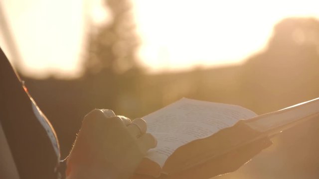 Silhouette of opening and closing book against sun on sunset.