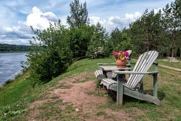 Wooden seats and table with flower pot are staying at coast of river. Latvia