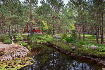 Beautiful park with small river and red bridge located between coniferous trees