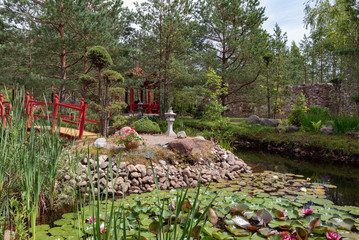 Beautiful park with small river and red bridge located between coniferous trees
