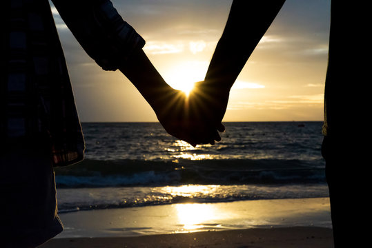 Symbols of love. silhouette Couple of man and woman hand holding together on sea and sky background during sunset for friendship day, love and valentines day concept
