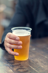 Man's hand holds a plastic pint of beer.