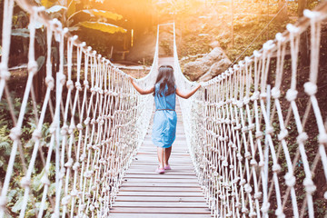 Cute asian child girl walking on the hanging rope bridge across the river in the forest with fun