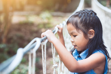 Cute asian child girl goes on the hanging rope bridge and looking down to the river