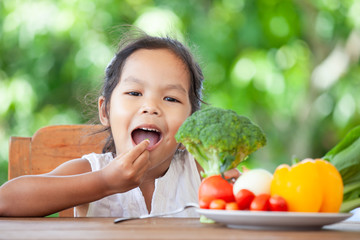 Cute asian child girl eating broccoli and learning about vegetables with happiness