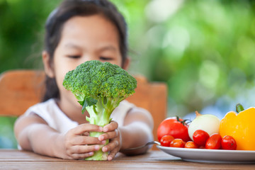 Cute asian child girl holding broccoli and learning about vegetables with happiness