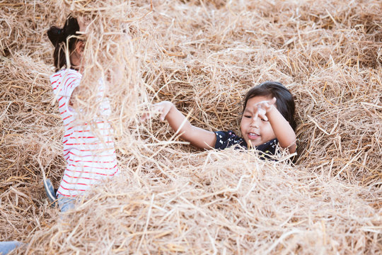 Two asian child girls having fun to play with hay stack together in the farm with happiness - Powered by Adobe