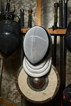 White protective HEMA mask and shield against the background of historical swords in a wooden rack for weapons