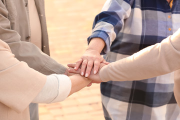 Senior people from care home putting hands together as symbol of unity outdoors