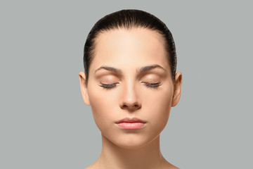 Young woman with natural eyebrows on grey background