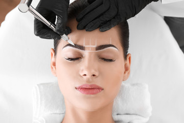 Young woman undergoing procedure of eyebrow permanent makeup in beauty salon - obrazy, fototapety, plakaty