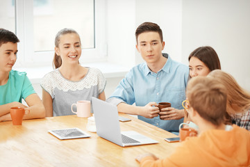 Group of cool teenagers with modern devices resting in cafe