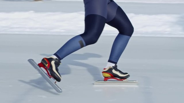 Slow motion shot of legs of two speed skaters in racing suits sprinting along track on outdoor ice rink in winter