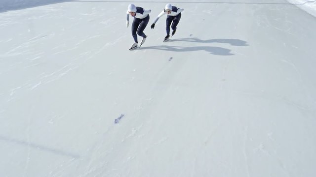 Front view of two professional athletes in racing suits and eyewear sprinting along track during speed skating practice on outdoor ice rink