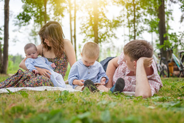 Naklejka na ściany i meble Young family with two young children on a summer picnic in the park on a beautiful sunny day