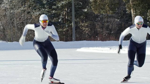 Front view of two sportswomen in racing suits and protective eyewear competing against each other in speed skating