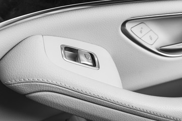 Car white leather interior details of door handle with windows controls and adjustments. Car window controls of modern car. Car detailing. Black and white