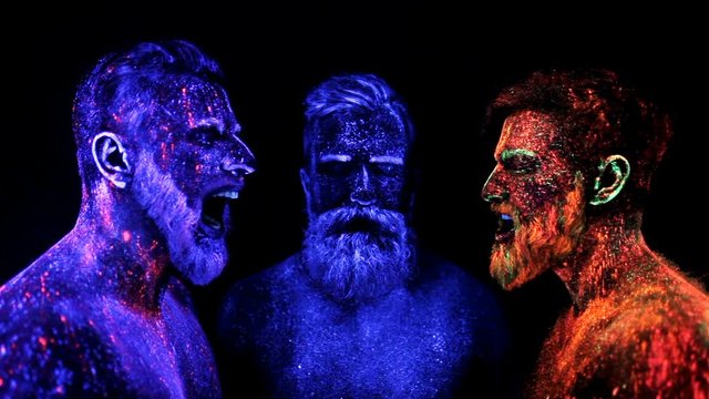 Three bearded men in UV powder are standing static
