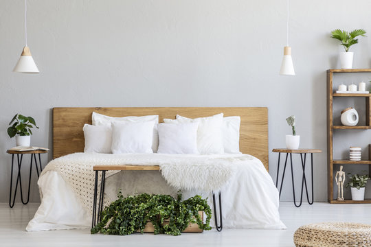 Lamps above wooden bed with white sheets in grey bedroom interior with pouf and plants. Real photo
