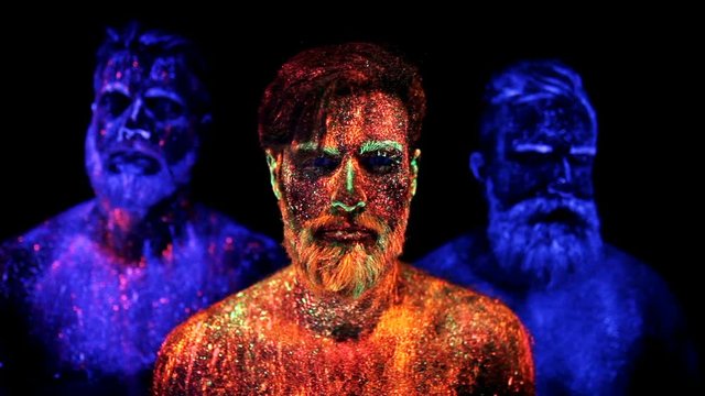Three bearded men in UV powder are standing static