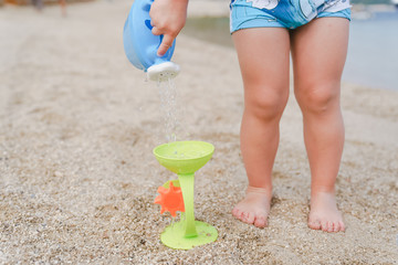 Child playing with toy watering can on beach