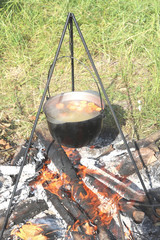 Cooking food in a kettle on a firewood fire at a picnic in summer in good clear weather