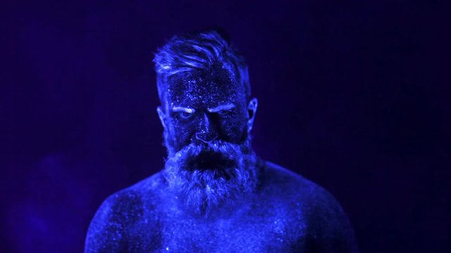 An evil man with a beard in the ultraviolet light is frighteningly screaming