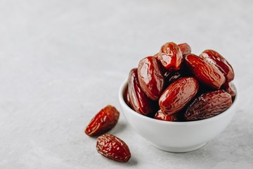 Dried dates in white bowl on grey background