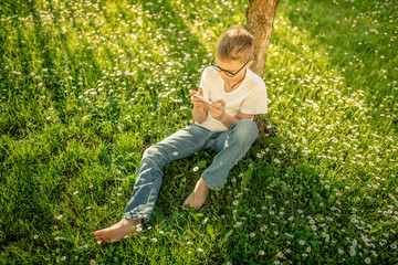 Young boy alone playing with smartphone. Pre teen with glasses sitting outdoor play with phone in hand. The use of the smartphone isolates the boy from the surrounding reality.