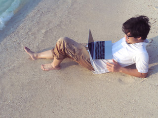 Relaxed young Asian man using laptop on the beach.