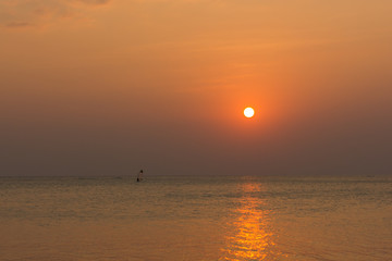 Person practicing windsurfing on the distance at warm sunset reflected on the calm sea in the island of Koh Phangan, Thailand. Summer holidays leisure activity, perfect vacation concepts