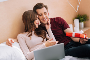 Enjoying you. Joyful female person keeping smile on her face while holding laptop on knees