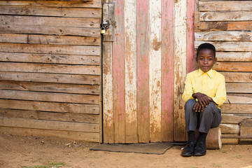 Little black boy sitting infront of a shack