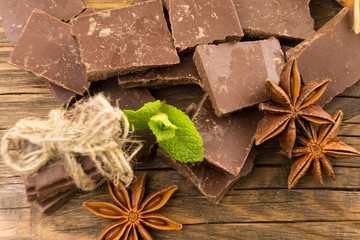 Pieces of chocolate, cinnamon and star anise on a wooden table.